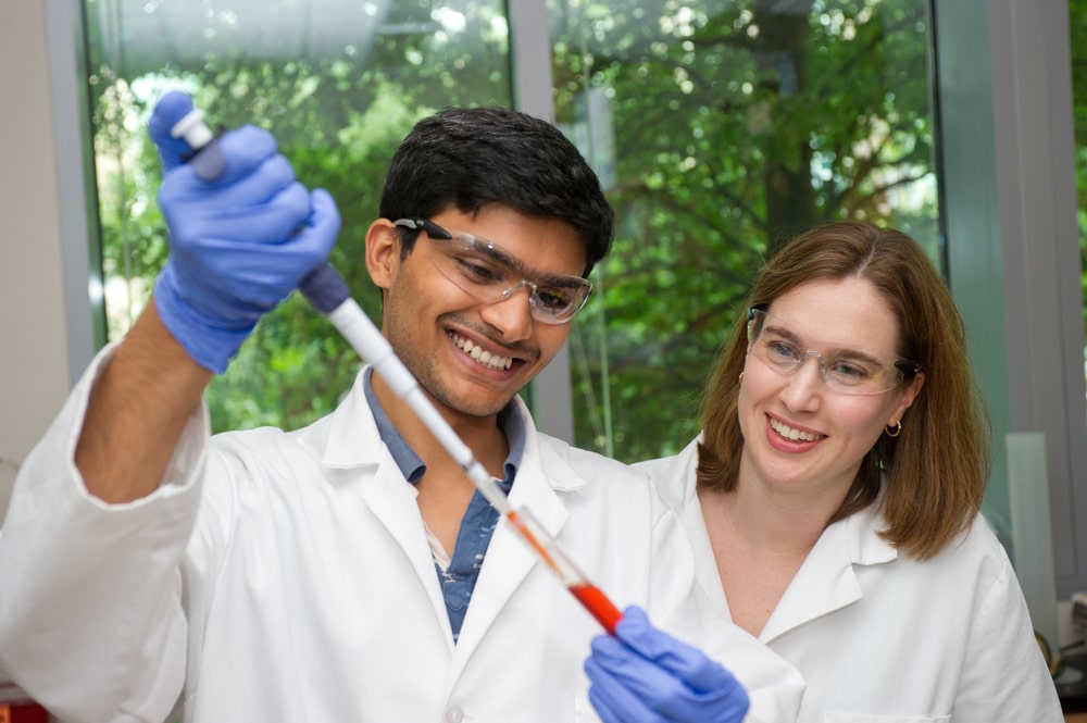 Research assistant using a pipette to transfer a liquid substance into a test tube while a professor observes