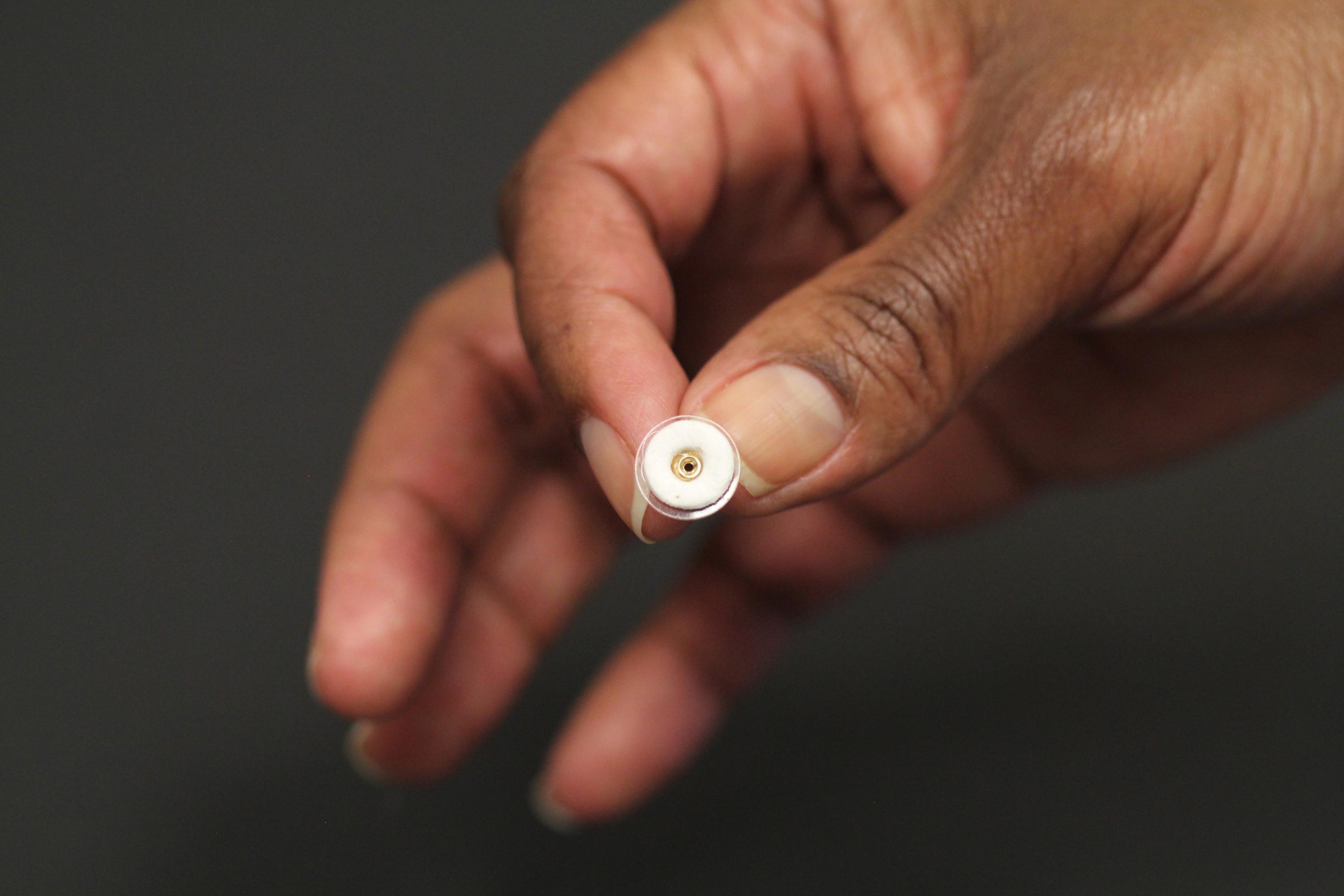 This photograph shows an earring patch (white) that can deliver contraceptive hormone while being worn on an earring back. The size of the patch is about one square centimeter. (Credit: Mark Prausnitz, Georgia Tech)