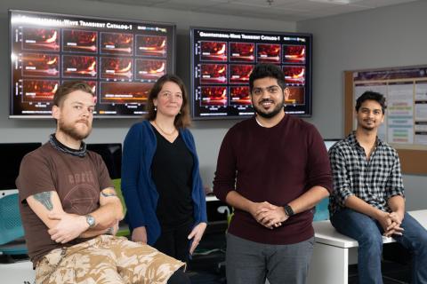 Georgia Tech LIGO researchers pose with a chart showing gravitational wave signals from cosmic events measured by LIGO-Virgo from 2015 to 2017. Shown are Research Scientist James Alexander Clark, Professor Lara Cadonati, Postdoctoral Fellow Karan Jani and Graduate Student Sudarshan Ghonge. (Credit: Allison Carter, Georgia Tech)