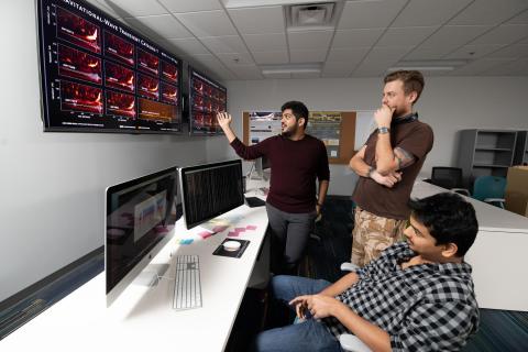 Georgia Tech LIGO researchers pose with a chart showing gravitational wave signals from cosmic events measured by LIGO-Virgo from 2015 to 2017. Shown are Postdoctoral Fellow Karan Jani, Research Scientist James Alexander Clark, and Graduate Student Sudarshan Ghonge. (Credit: Allison Carter, Georgia Tech)